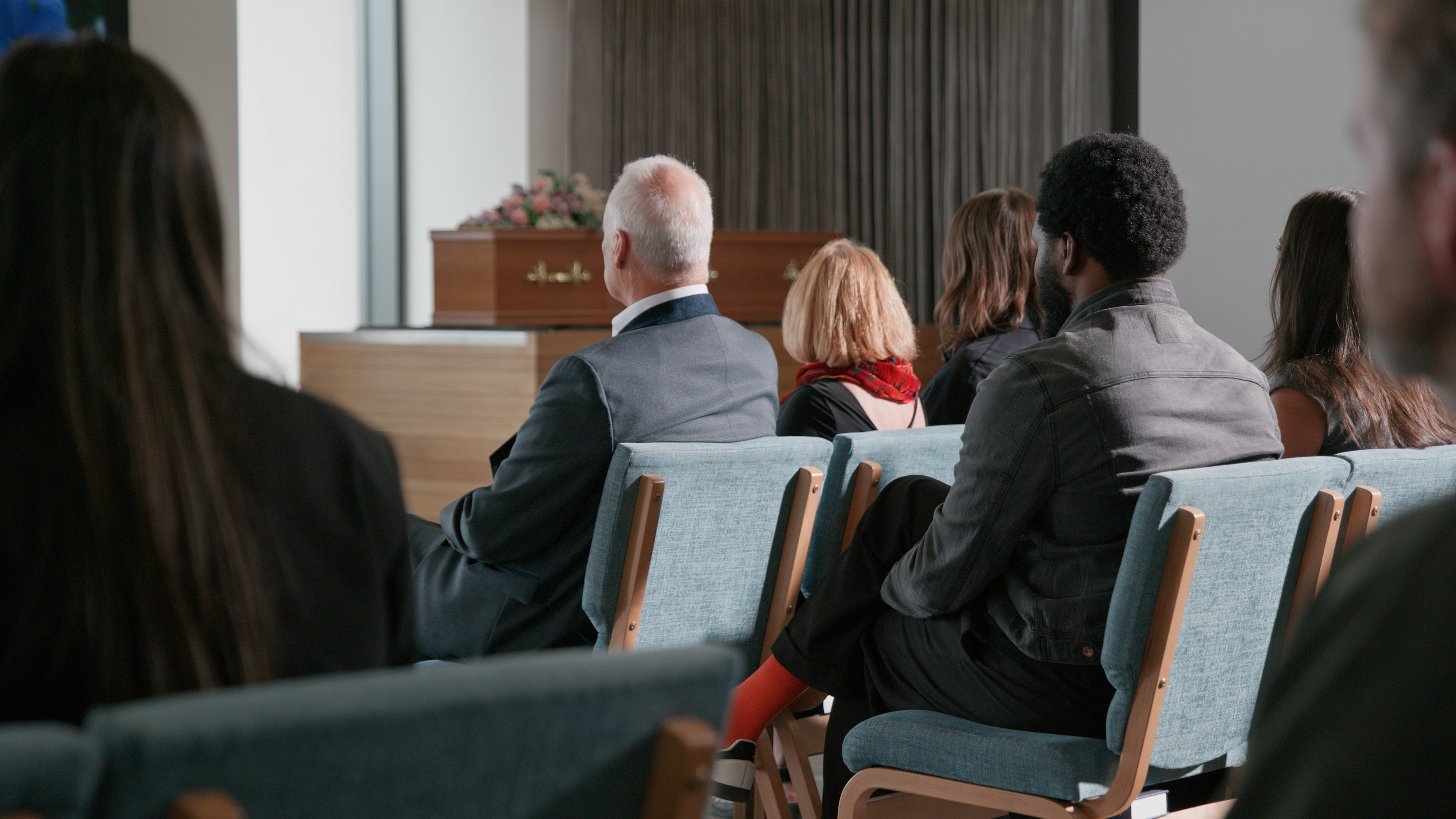 Mourners seated in rows of chairs facing a coffin at the front of a modern chapel.