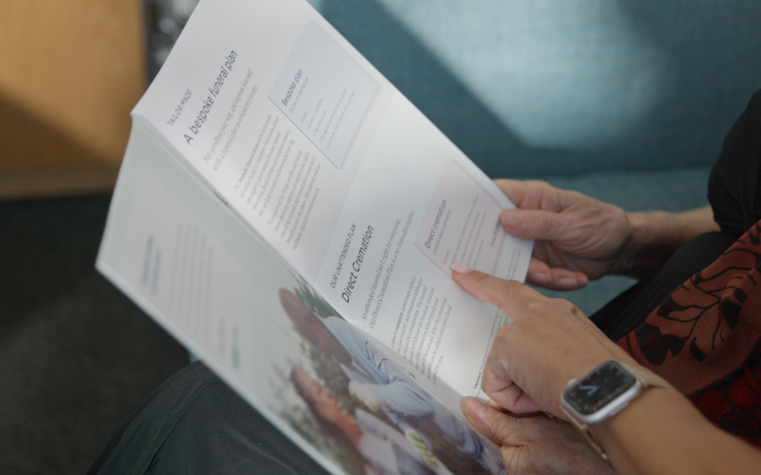 Two people holding open a printed funeral plan brochure, reading the pages together.
