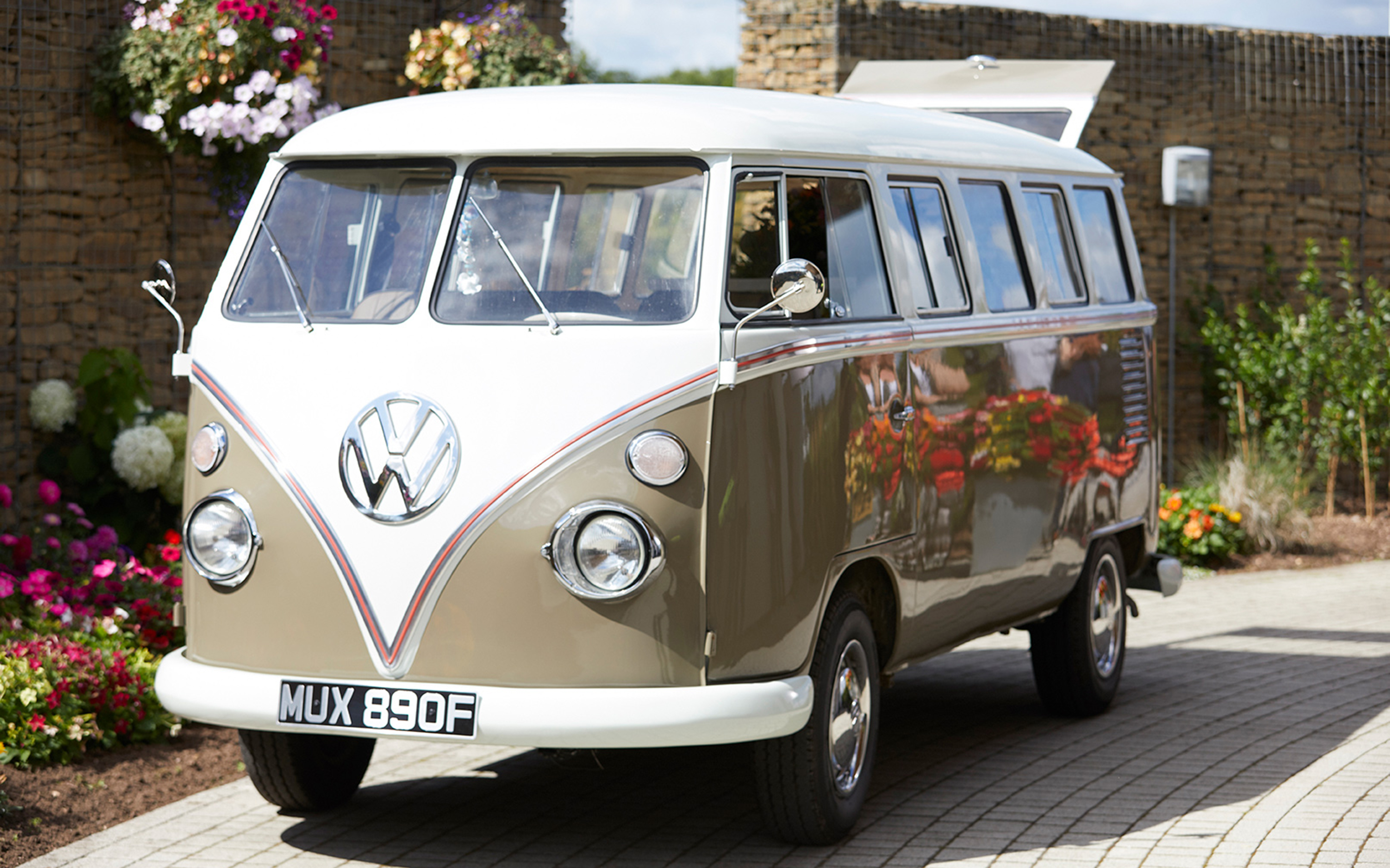 A vintage cream and green Volkswagen camper van parked on a driveway beside flower beds.