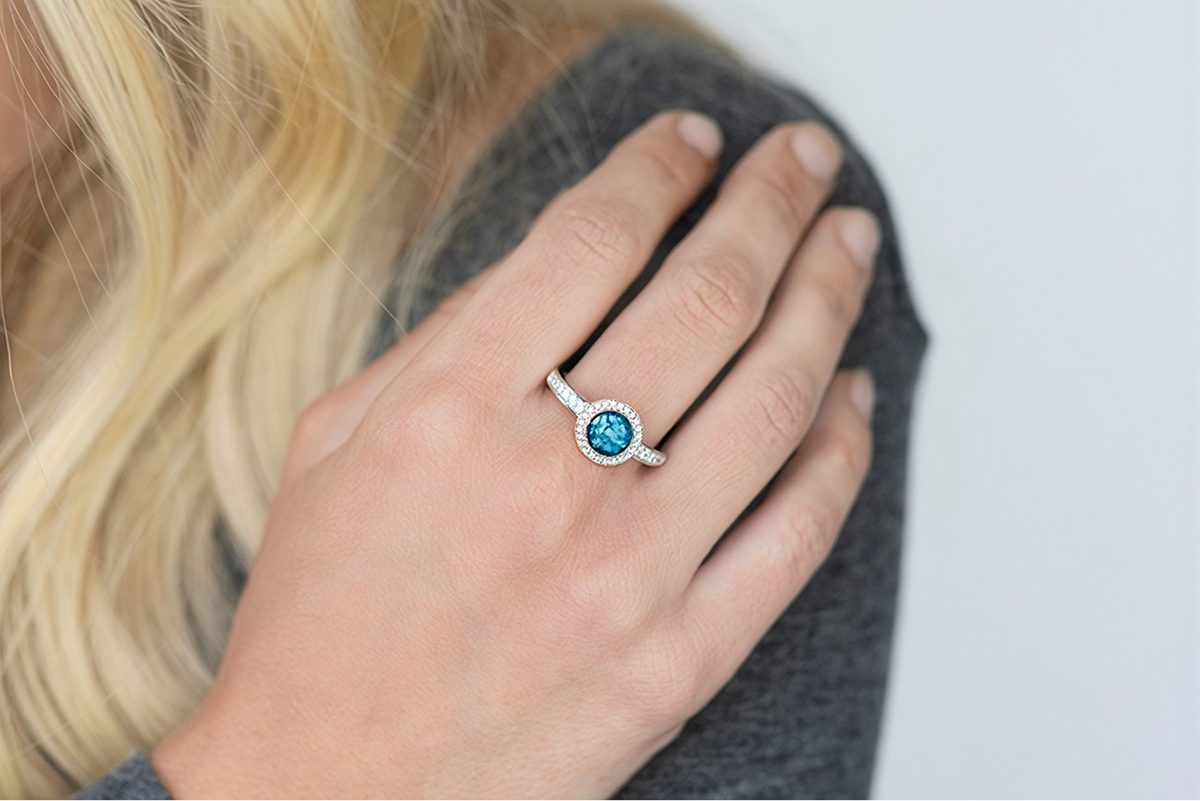 A hand wearing a silver ring set with a blue stone, resting on a grey knitted shoulder.