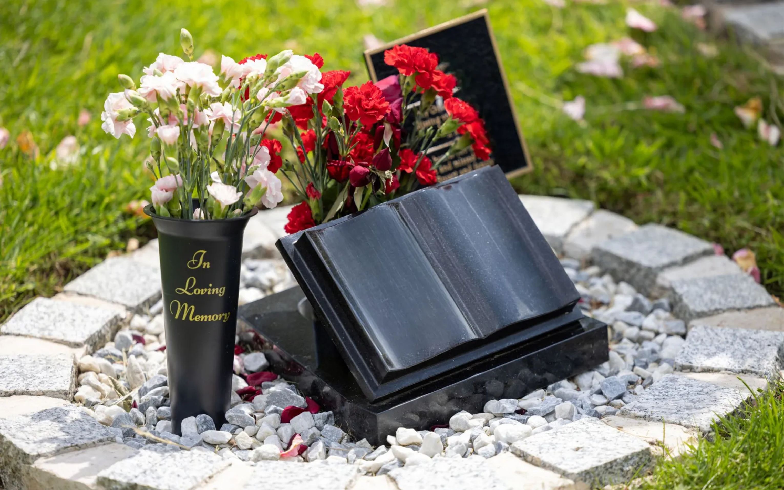 A black granite open-book memorial with red and white carnations in a memorial vase.