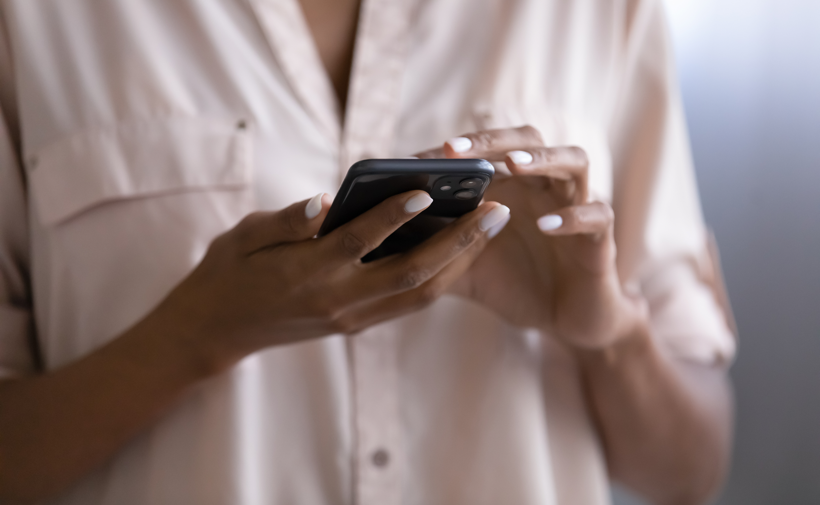 Close up of a person in a cream shirt holding a smartphone in both hands.