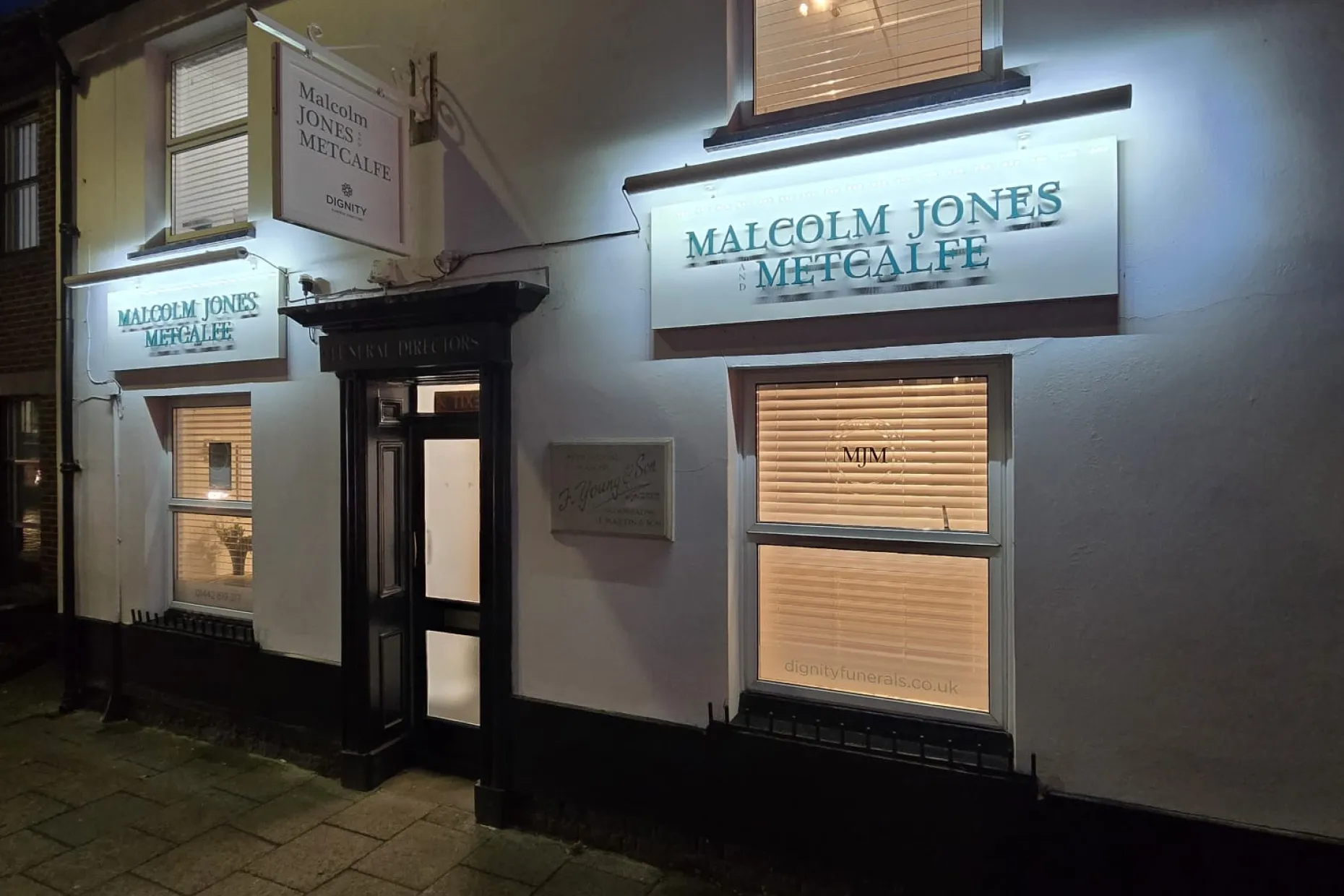 Malcolm Jones & Metcalfe Funeral Directors branch on High Street, Berkhamsted, lit at dusk.