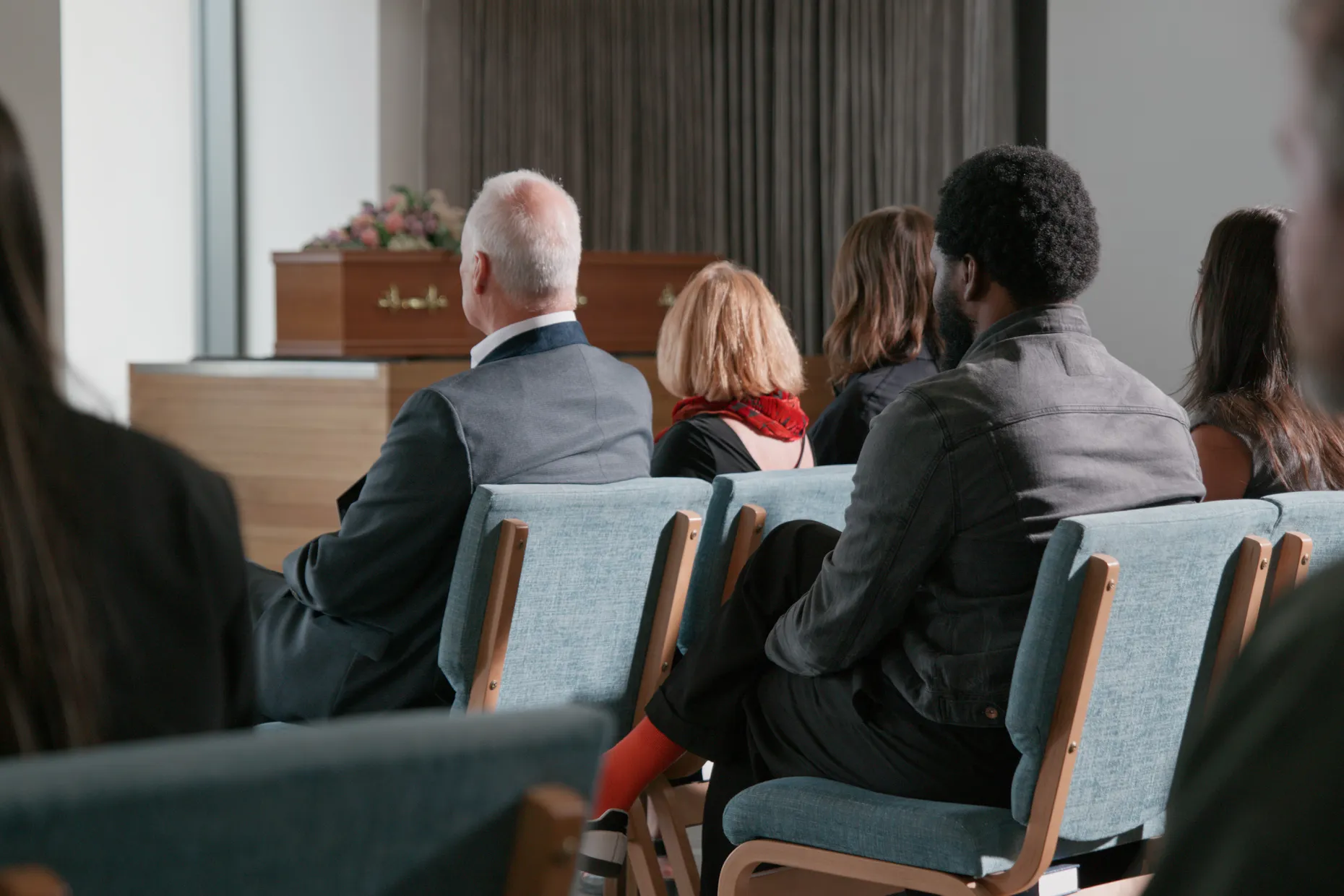 Mourners seated in rows of chairs in a chapel, facing a coffin at the front.
