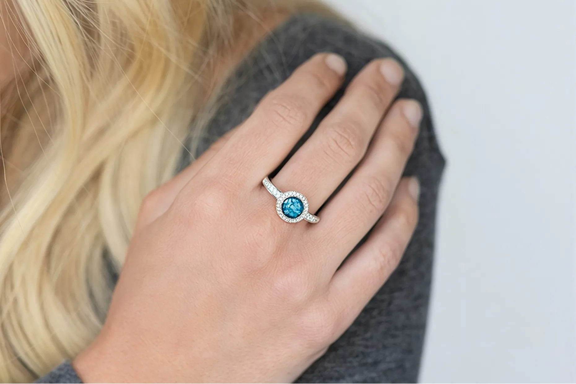A hand wearing a silver ring set with a blue stone, resting on a grey knitted shoulder.