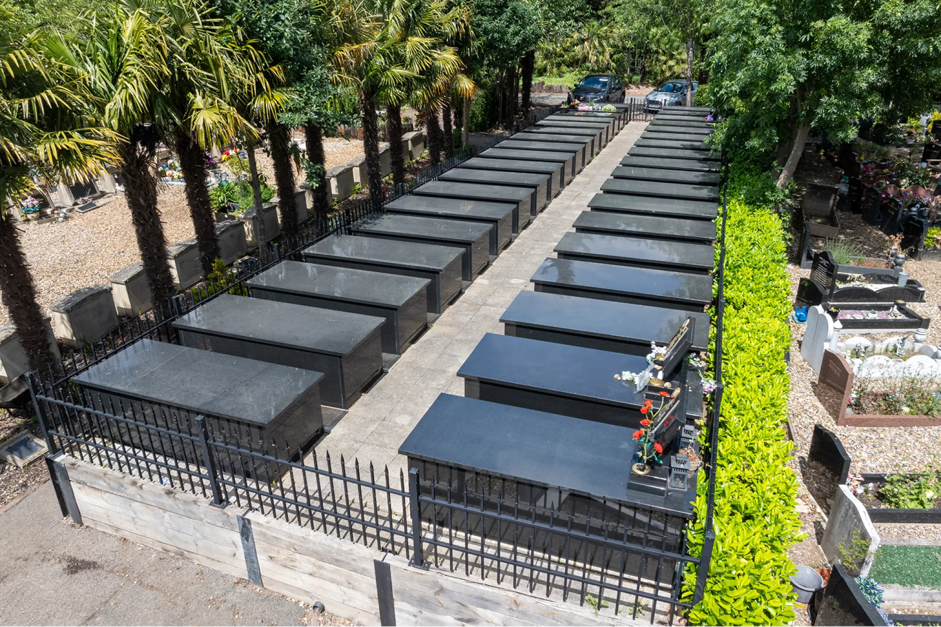 Rows of polished black granite burial vaults behind iron railings, with trees and hedging around them.