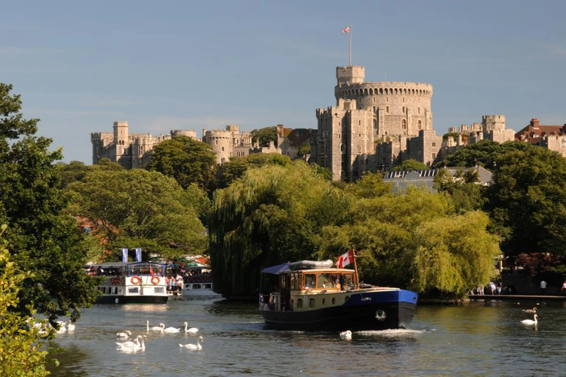 Windsor Castle seen above the River Thames, with boats and swans on the water